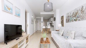 A modern living room with a flat-screen TV, wooden entertainment unit, and a white sofa. - Home2Book Esmeralda Beach, Resid. Playa Paraíso (Pajara)