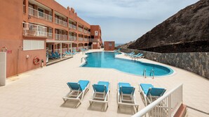 A swimming pool with blue lounge chairs, a lifebuoy, and a building with balconies. - Home2Book Esmeralda Beach, Resid. Playa Paraíso (Pajara)
