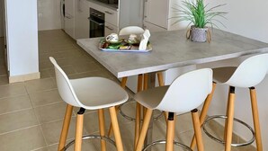 A modern kitchen with white cabinets, a dining table with four chairs, and a clock on the wall. - Home2Book Esmeralda Beach, Resid. Playa Paraíso (Pajara)