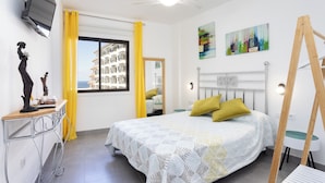 A bedroom with a bed, a desk, a mirror, and a window with yellow curtains. - Home2Book Sunset Terrace & Pool Haven (Puerto Santiago)