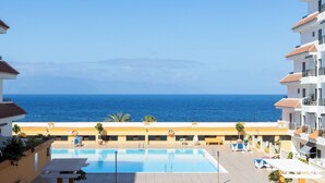 A swimming pool with a view of the sea, surrounded by buildings with balconies. - Home2Book Sunset Terrace & Pool Haven (Puerto Santiago)