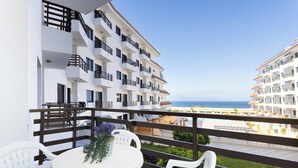 A balcony with a white table and chairs, a potted plant, and a view of the sea and other buildings. - Home2Book Sunset Terrace & Pool Haven (Puerto Santiago)