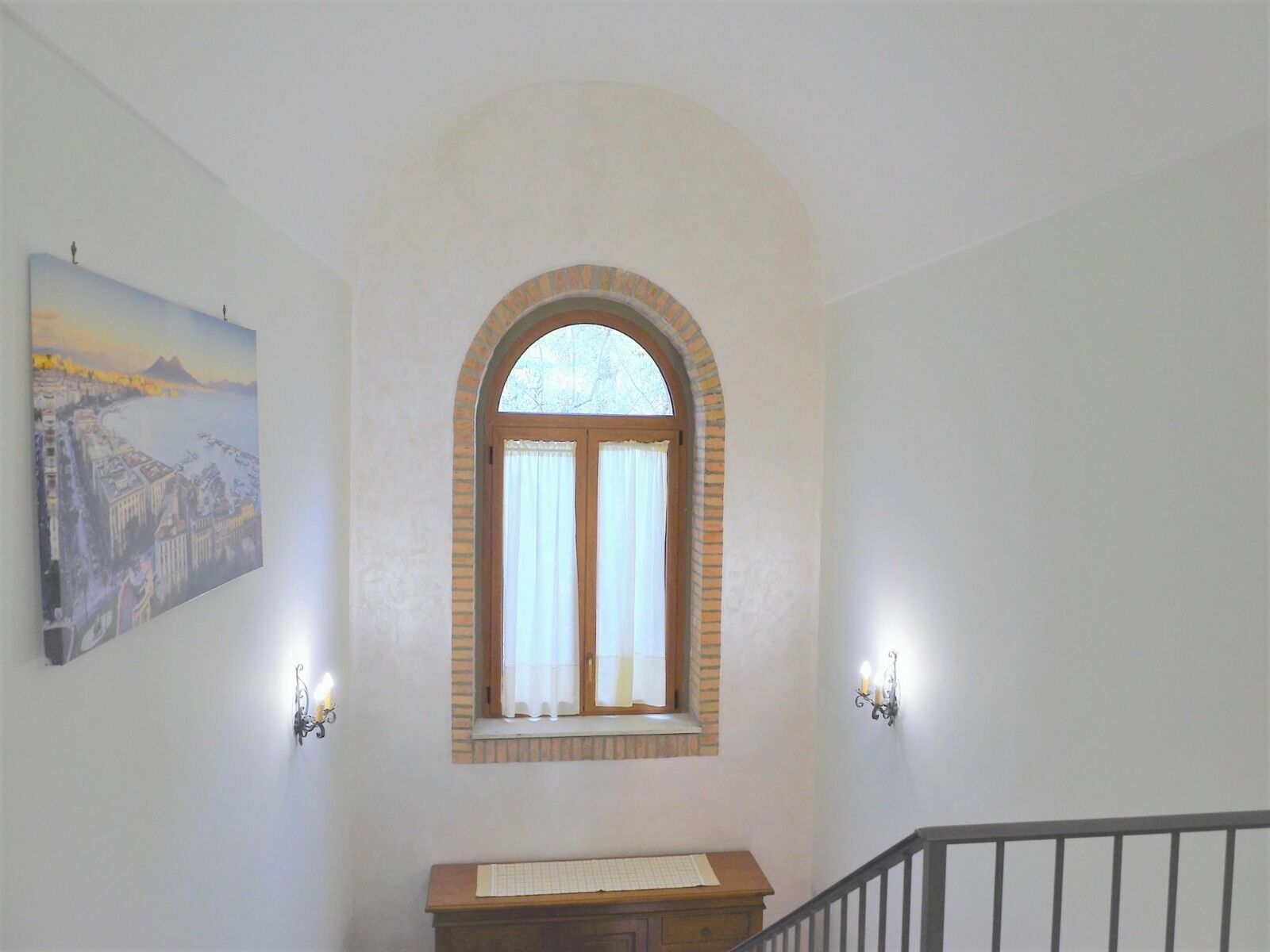 Eine Treppe mit hölzernem Geländer, ein kleiner Tisch mit einer Tastatur und ein Stadtbild als Gemälde.