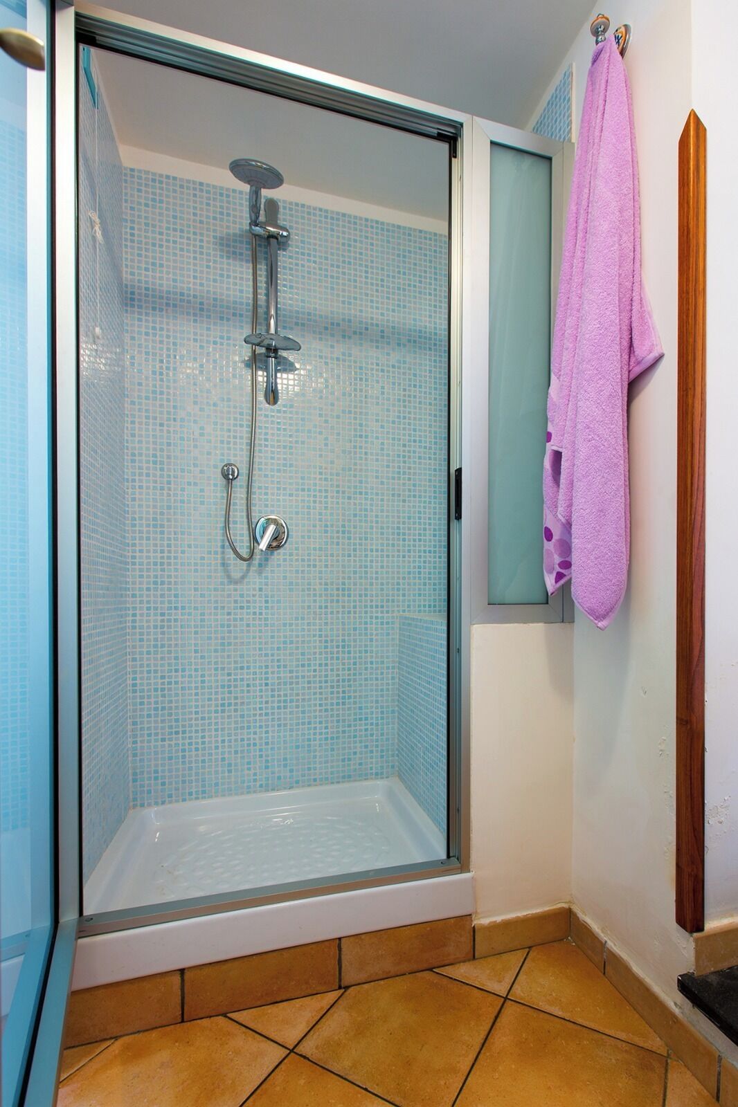 A glass-enclosed shower with a tiled floor and a pink towel hanging on the wall.