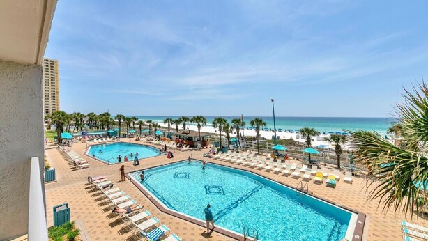 A resort with two swimming pools, beach umbrellas, lounge chairs, and a view of the ocean. - The Summit 312 (Panama City Beach)