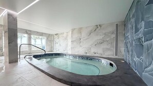 A modern indoor swimming pool with a marble wall and ceiling, a clear glass barrier, and a tiled floor. - The Summit 312 (Panama City Beach)