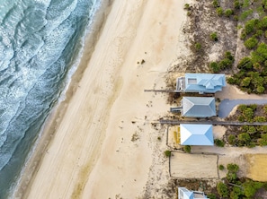 An aerial view of a beachside property with a wooden pier leading to a cluster of buildings with blue roofs.