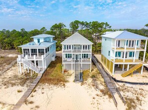 Una propiedad frente a la playa con tres casas de varios pisos conectadas por una pasarela de madera.