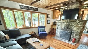 Un salon chaleureux avec une cheminée en pierre, un canapé, une table basse et une pancarte sur laquelle on peut lire : « Bienvenue au bord du lac ».