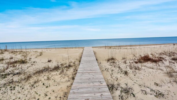 A wooden boardwalk leading to a beach with sand dunes and sparse vegetation. - Palmetto Breeze (Port St. Joe)