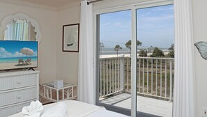 A bedroom with a large sliding glass door to a balcony, a television, a dresser, and a framed picture. - Palmetto Breeze (Port St. Joe)