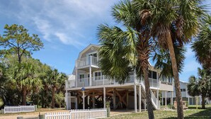 A two-story house with a balcony, surrounded by palm trees and a white picket fence. - Palmetto Breeze (Port St. Joe)