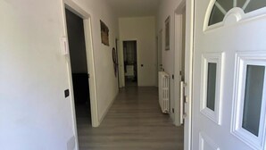 Un couloir avec un plancher en bois et des murs blancs. Il y a une porte sur la droite, dotée d’un panneau en verre.