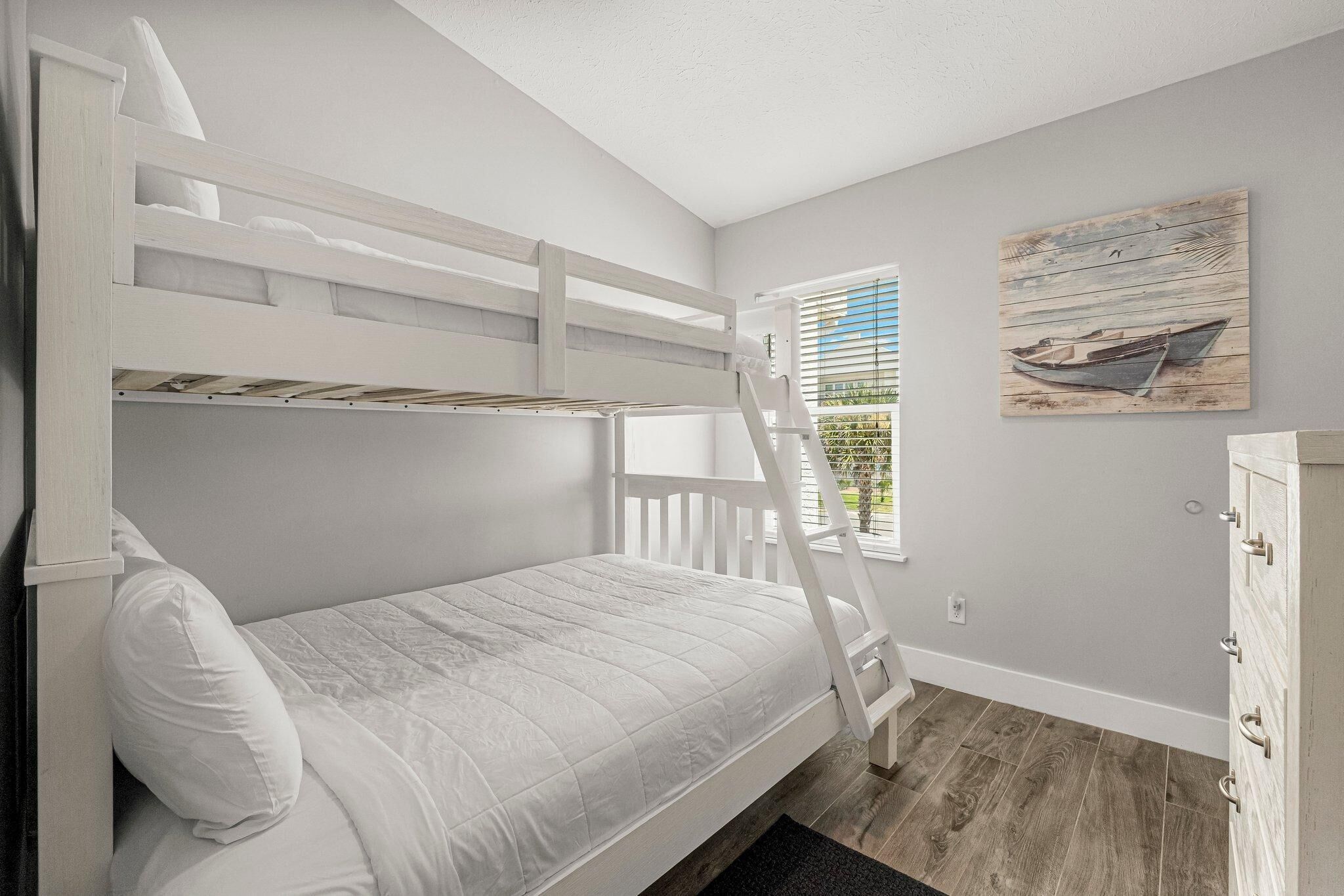 A bunk bed with a ladder, a window with blinds, and a wooden floor.