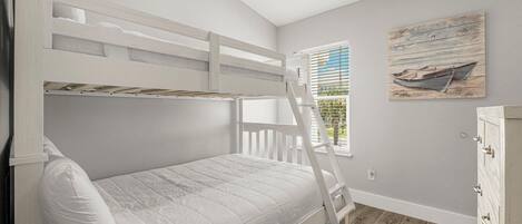 A bunk bed with a ladder, a window with blinds, and a wooden floor.