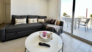 Una sala de estar moderna con un sofá gris, una mesa de centro redonda blanca y un balcón con mobiliario exterior.
