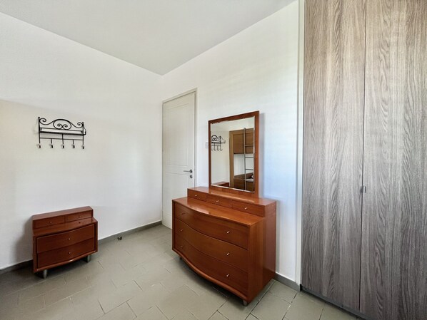 A bedroom with a wooden dresser, a mirror, a wardrobe, and a wall-mounted coat rack.