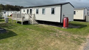 A single-story mobile home with a front deck and a staircase leading to the entrance. - Seaside Caravan in Eyemouth (Eyemouth)