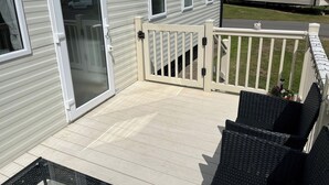 A mobile home with a sliding door, a small deck with outdoor furniture, and a fenced area. - Seaside Caravan in Eyemouth (Eyemouth)