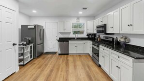 A modern kitchen with white cabinets, a black countertop, and a wooden floor. - TCU Area Home - Blue Bonnet Circle (Fort Worth)