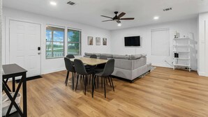 A modern living room with a dining area, grey sofa, flat-screen TV, and ceiling fan. - TCU Area Home - Blue Bonnet Circle (Fort Worth)