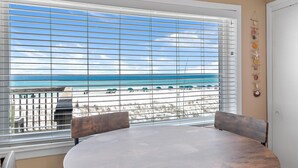 A room with a large window overlooking a beach, a round table, and two chairs. - Capri on the Gulf 108 (Destin)