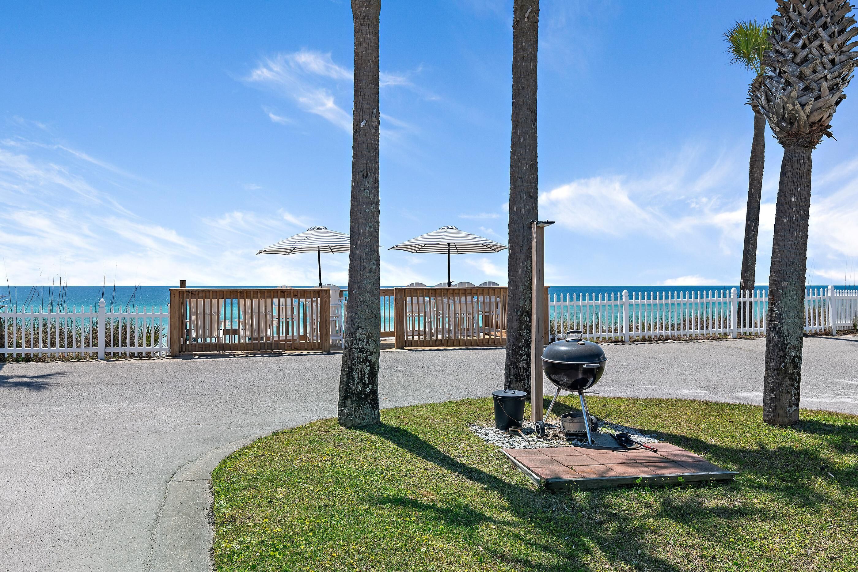 Un vialetto lastricato conduce a una spiaggia con palme, un barbecue e ombrelloni.