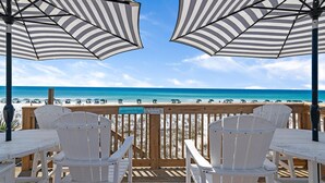 A wooden deck with white chairs and striped umbrellas overlooking a beach. - Capri on the Gulf 108 (Destin)