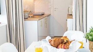 A modern kitchen with white cabinets and a wooden countertop. There is a breakfast setup on the dining table with croissants and orange juice. - Elegant Apt between sea, ponds and nature, 5 minutes from beaches, direct access to streetcar. (Pérols)