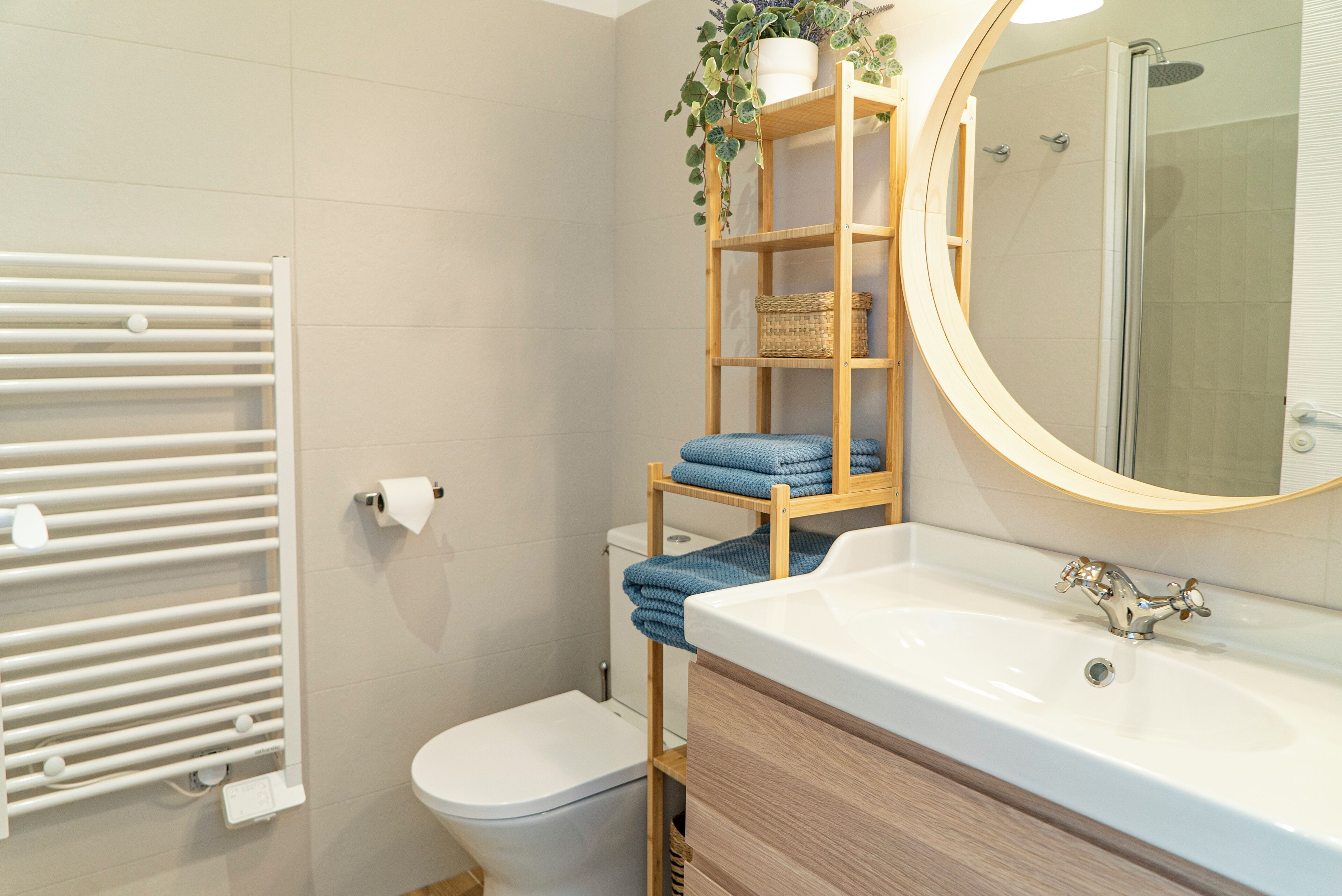 A bathroom with a white toilet, a wooden shelf with towels, a white sink, and a mirror.
