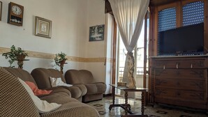 A living room with patterned sofas, a wooden cabinet, a television, and a decorative statue. - Sicilian Apt in Donnalucata-sleeps 4- 2 Min Beach (Scicli)