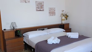 A neatly made bed with white linens and a purple blanket, a wooden nightstand with a lamp and a plant, and a vase with flowers on the wall. - Sicilian Apt in Donnalucata-sleeps 4- 2 Min Beach (Scicli)