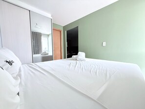Quarto de hotel com cama, janela com cortinas, porta e parede com interruptor de luz.