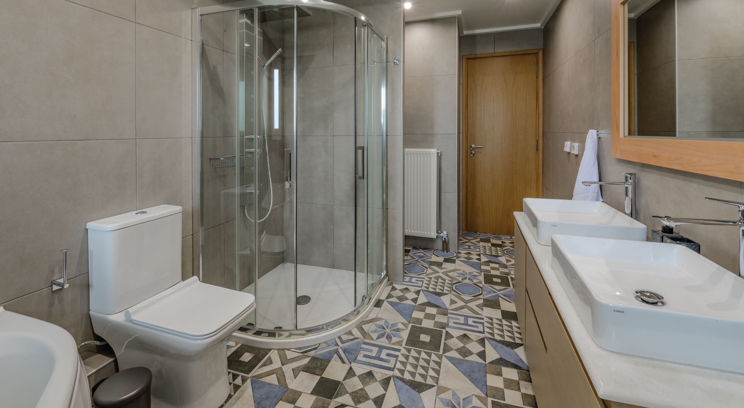 A modern bathroom with a glass-enclosed shower, a toilet, and two sinks.