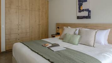 Una cama bien hecha con una manta verde, una mesita de noche con una lámpara y un armario de madera.