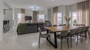 A modern living room with a sofa, dining table, and chairs. There is a TV and a fireplace. - Jaax Apartment Airport by Airstay (Spata-Artemida)