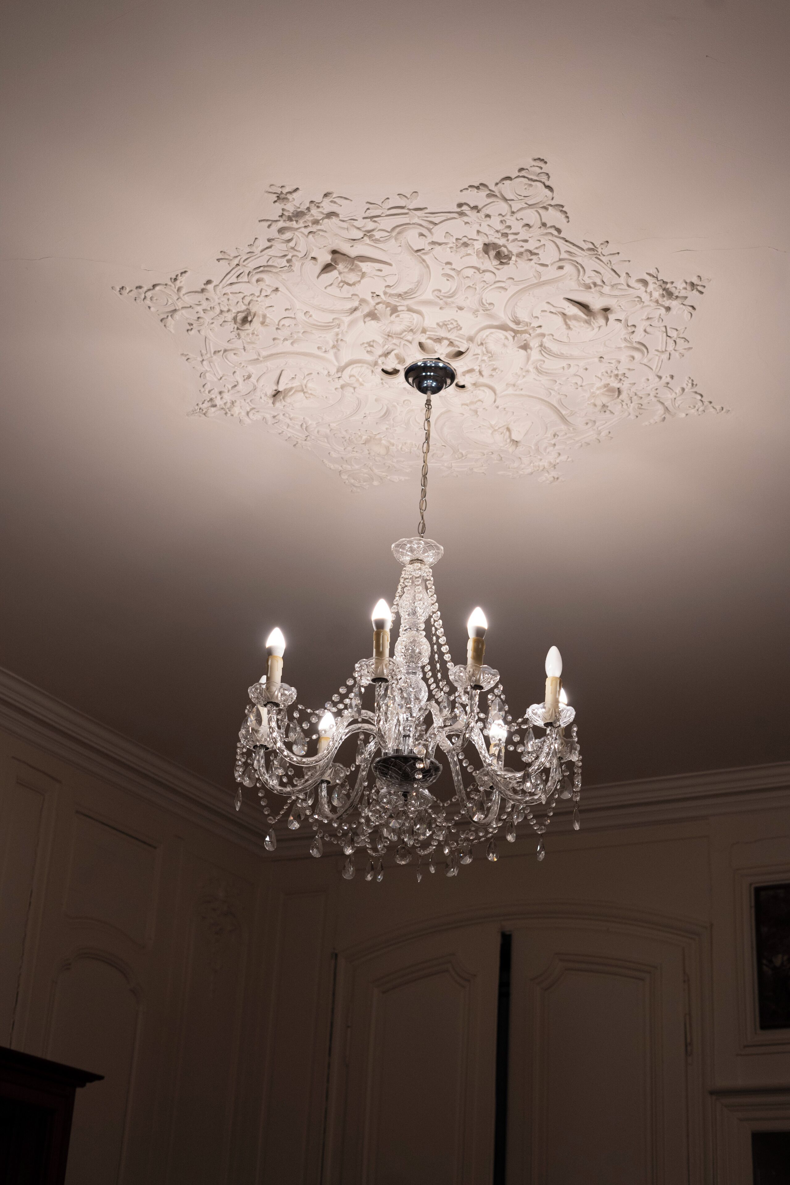 Un lustre orné de plusieurs lampes en forme de bougies, un plafond décoratif et une pièce avec des boiseries et un tableau encadré.