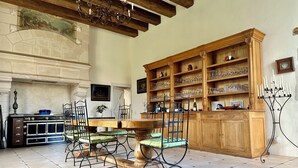 Een eethoek met een houten tafel, stoelen en een grote kast vol met kristal.