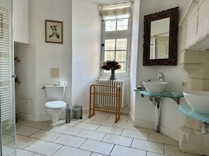 Un baño con inodoro, bidé, lavamanos de vidrio y un espejo.