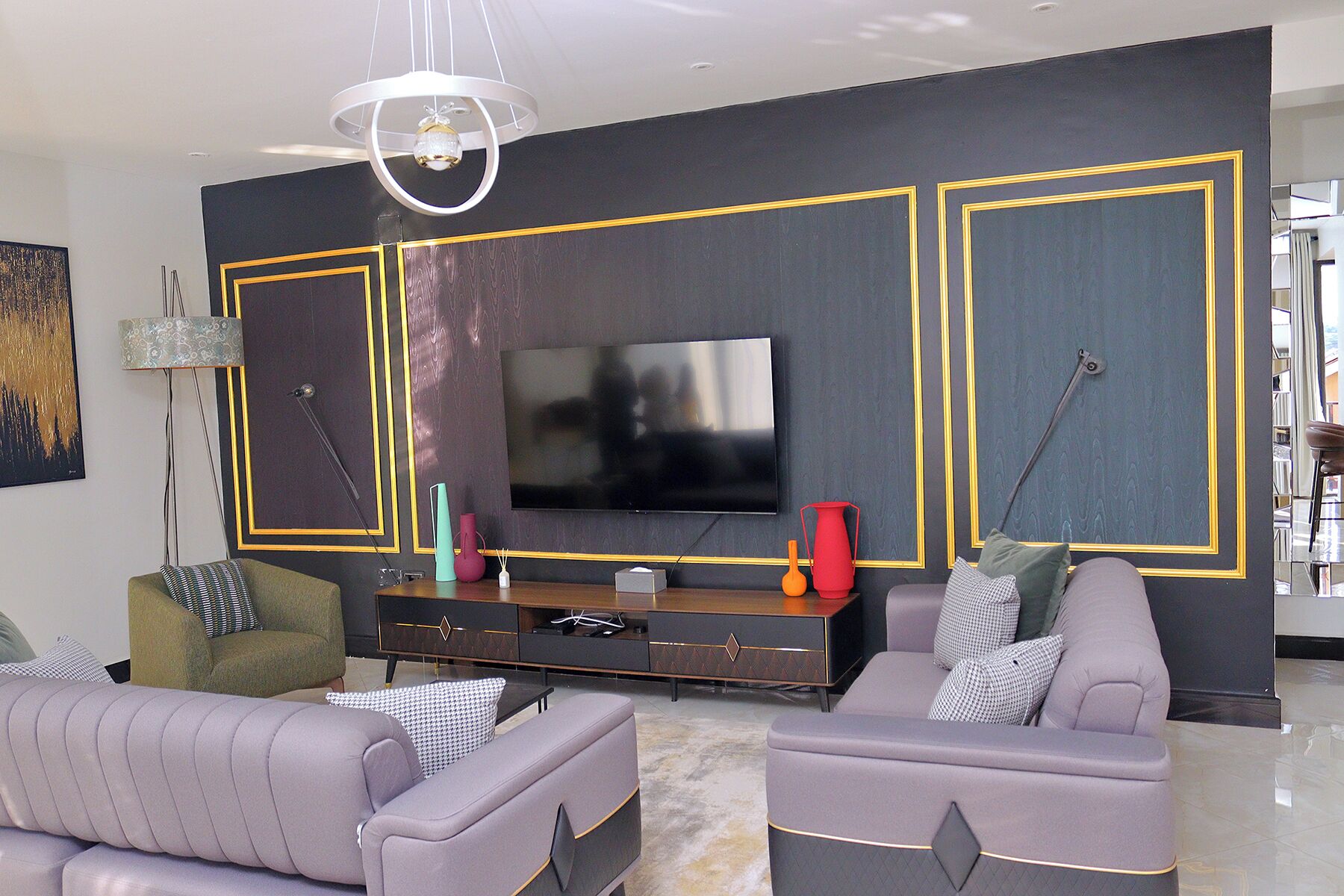 A modern living room with a large flat-screen TV mounted on a dark wall with yellow trim. There are two sofas, a coffee table, and a floor lamp.