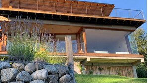 A modern house with a wooden deck, large windows, and a stone wall. - Tanière. Contemporary design house. Breathtaking lake view. (Villa La Angostura)