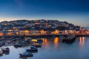 A coastal town at dusk with boats docked in the harbor and buildings along the waterfront.