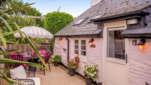 A cozy patio area with outdoor seating, a white door, and potted plants. - 3 Bed in Brixham (oc-r31919) (Brixham)