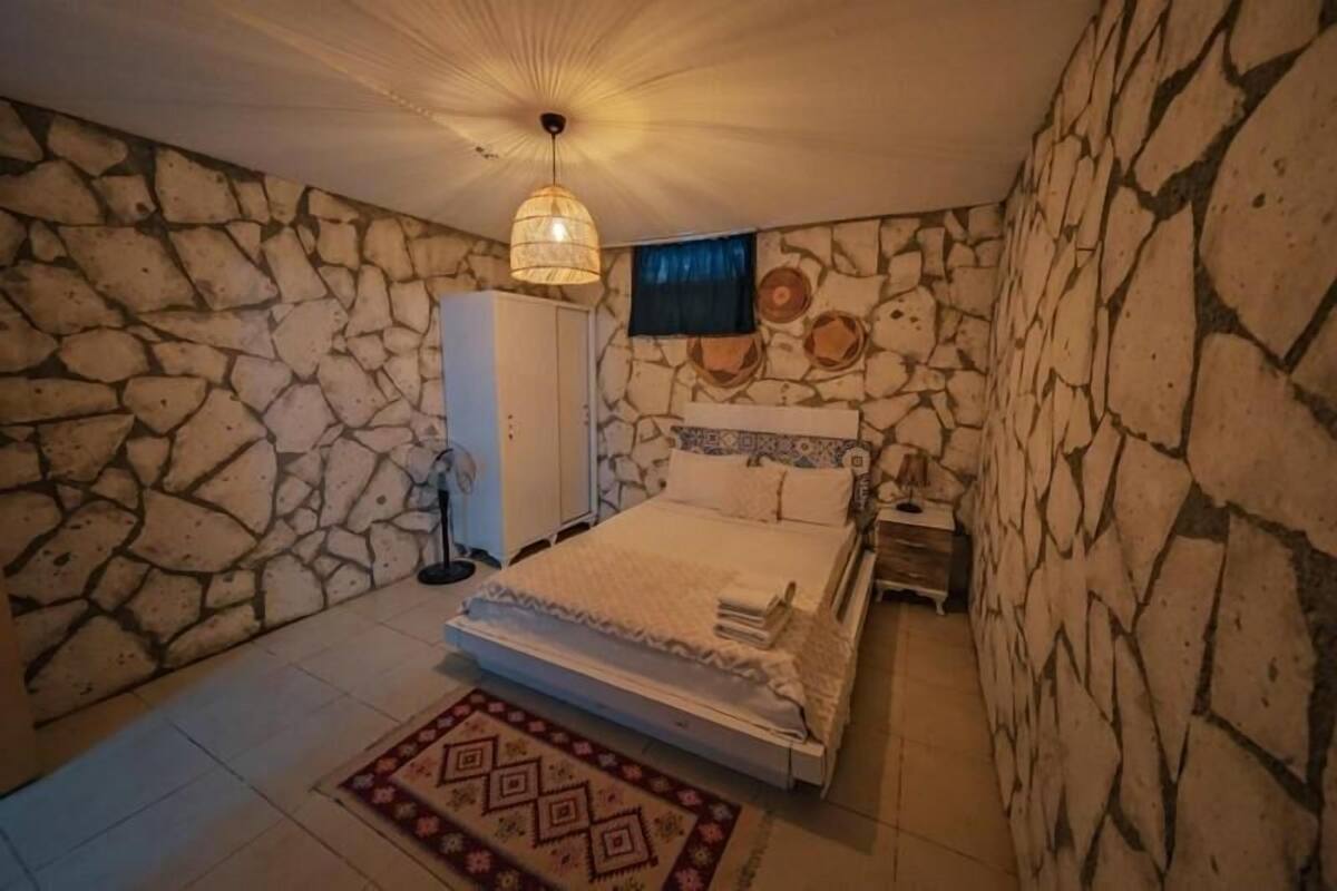 A bedroom with a stone wall, a bed, a nightstand, a wardrobe, and a hanging light fixture.