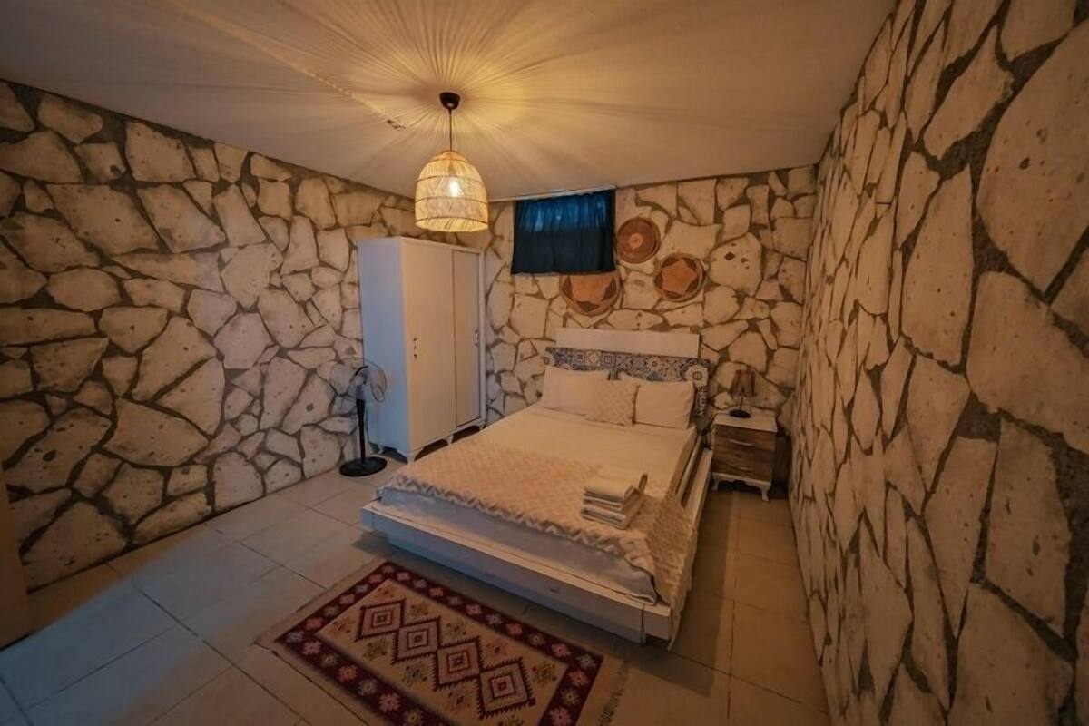A bedroom with a stone wall, a bed, a wardrobe, and a television.
