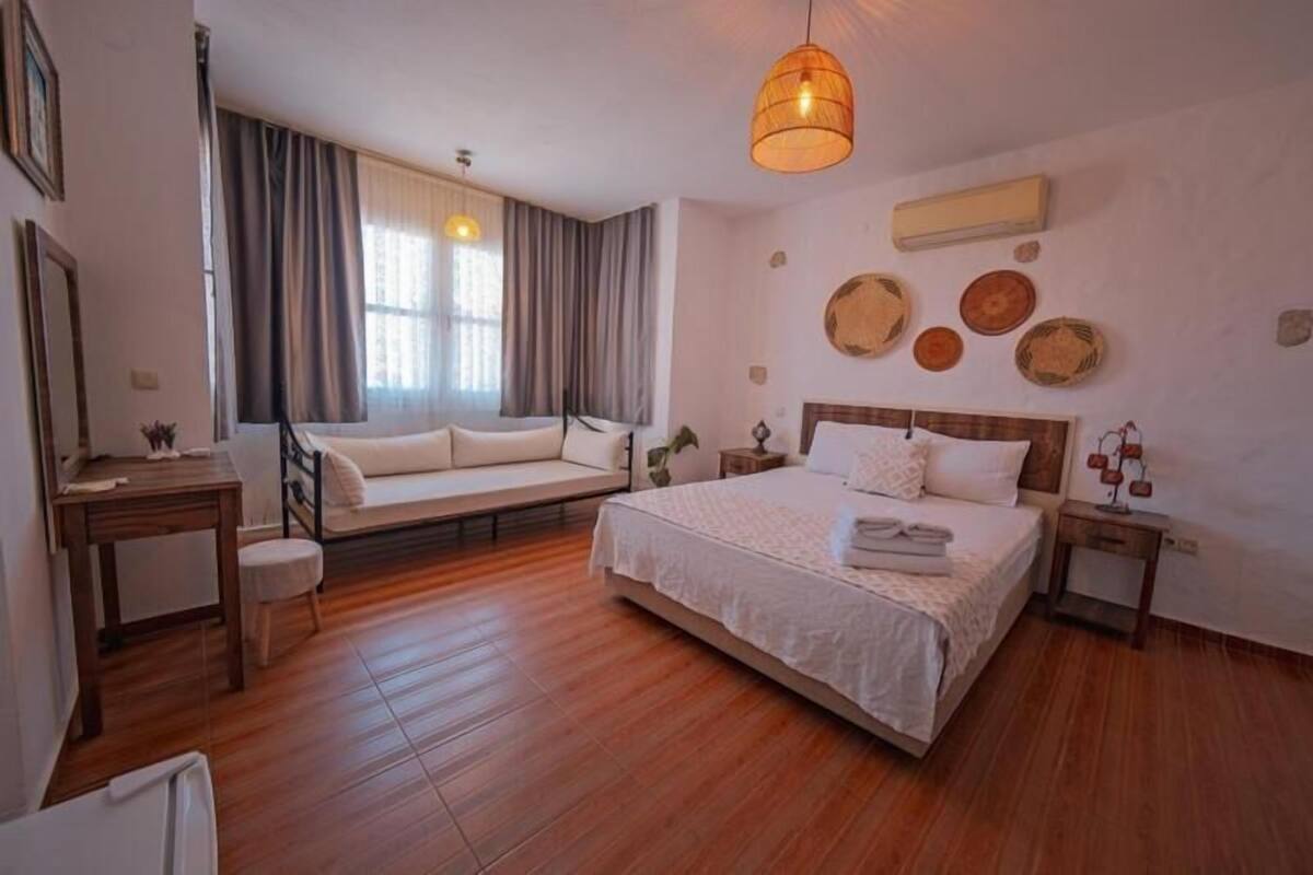 A bedroom with a bed, bedside tables, a sofa, a desk, and a hanging light fixture.