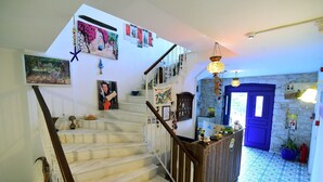 Una escalera conduce a una habitación con una puerta azul, decorada con diversas obras de arte en las paredes y una lámpara colgante.