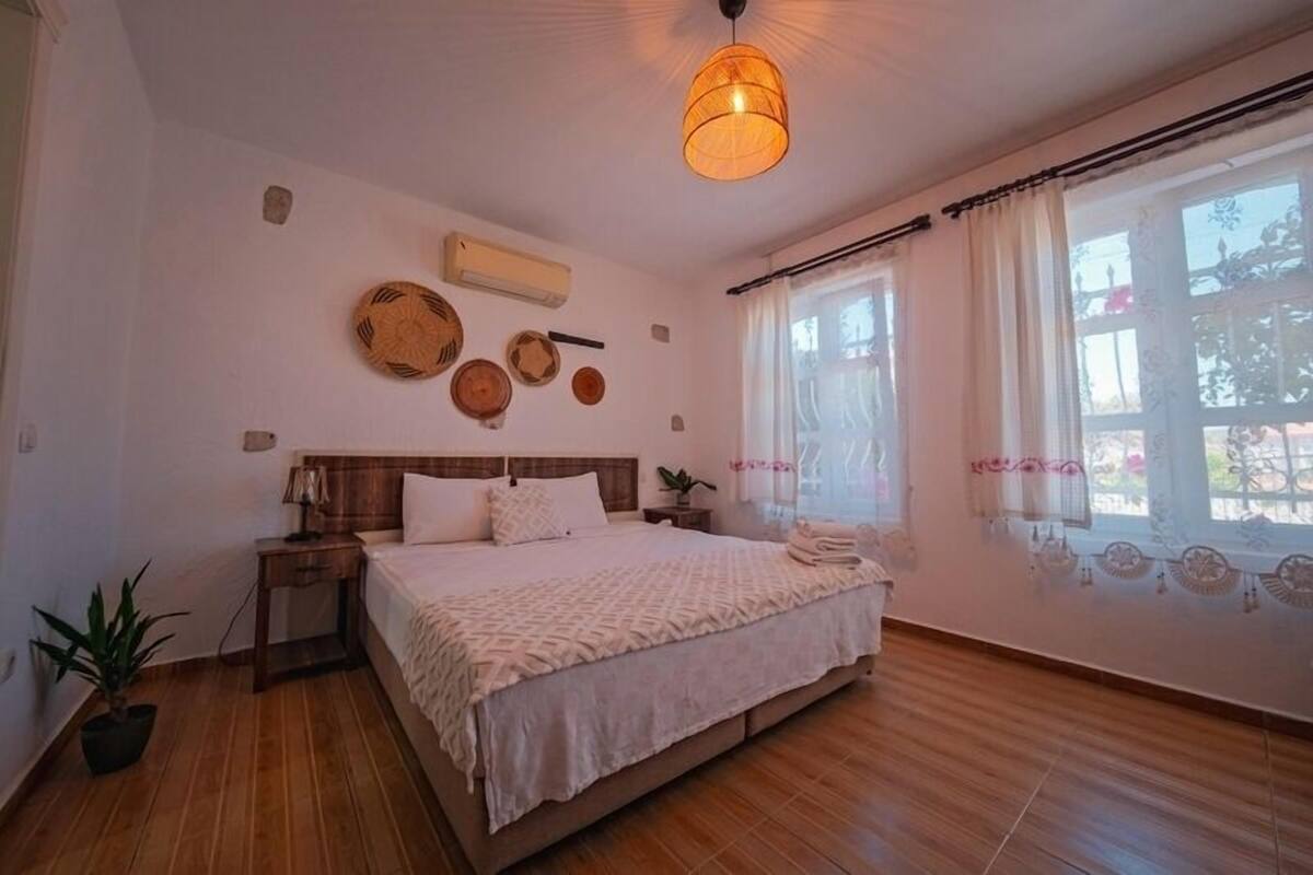A bedroom with a wooden bed, a bedside table, a hanging light fixture, and a window with curtains.