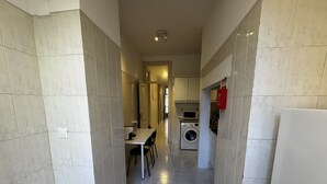 A narrow kitchen with a washing machine, a microwave, and a dining area with chairs. - Terrace Marquês (Lisbon)