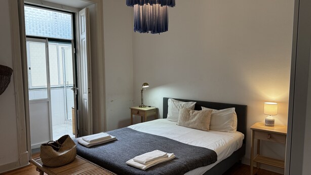 A bedroom with a bed, bedside tables, a bench, and a hanging light fixture. - Terrace Marquês (Lisbon)